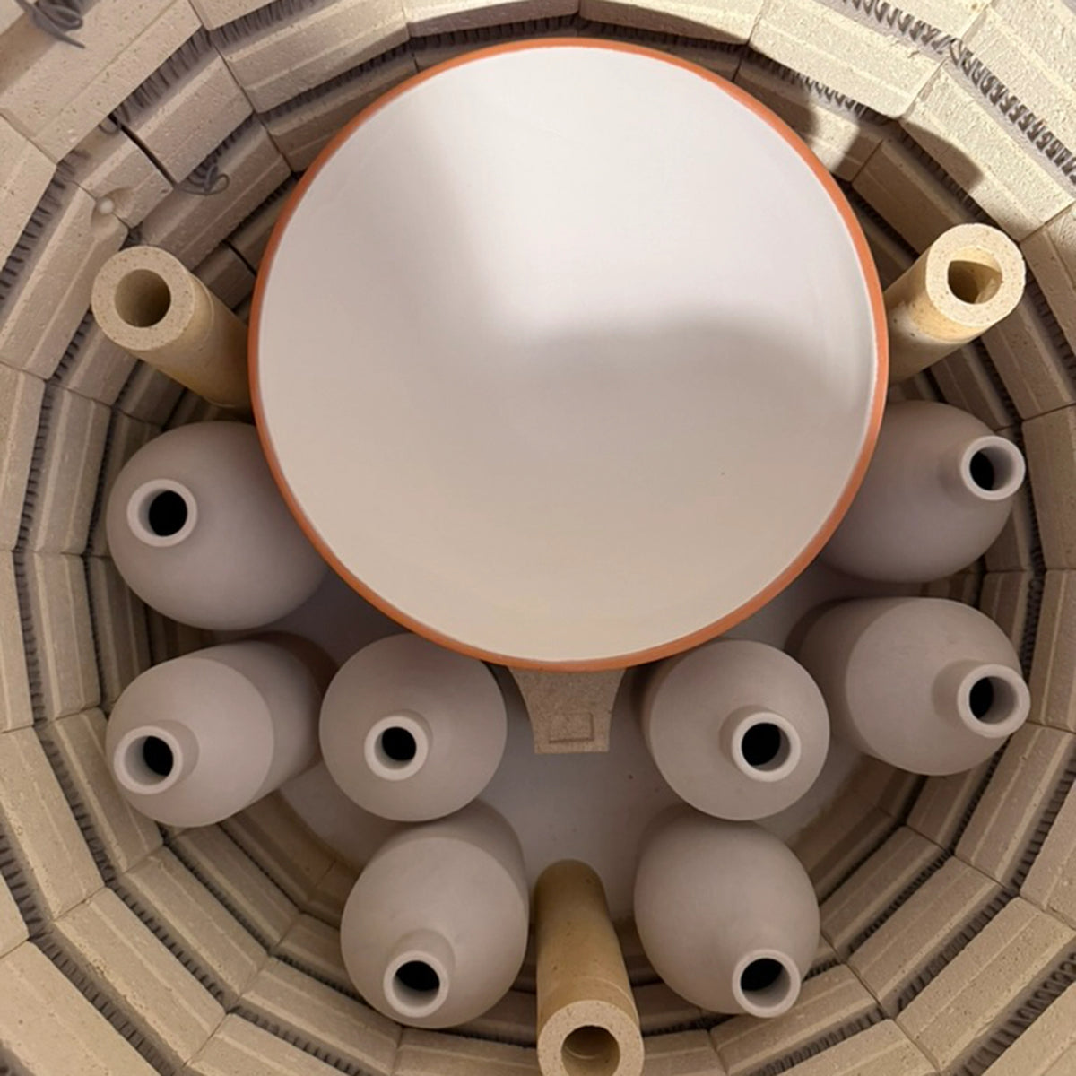 Een bovenaanzicht in een oven toont verschillende handgedraaide, ongeglazuurde vazen en de AB Ceramics Olijfolie Fles Grijs Opaal 84 cl op ovenplanken - ideaal voor het maken van unieke keukenaccessoires van AB Ceramics.