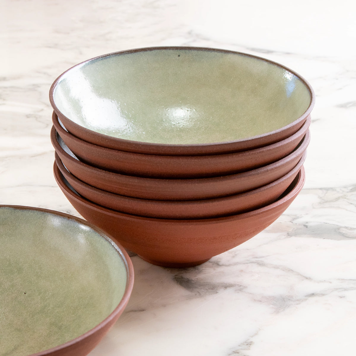 Een stapel van vijf AB Ceramics Noodle Kom Rood Mint D19 kommen staat op een wit marmeren oppervlak, met één bijpassende kom apart ervoor.