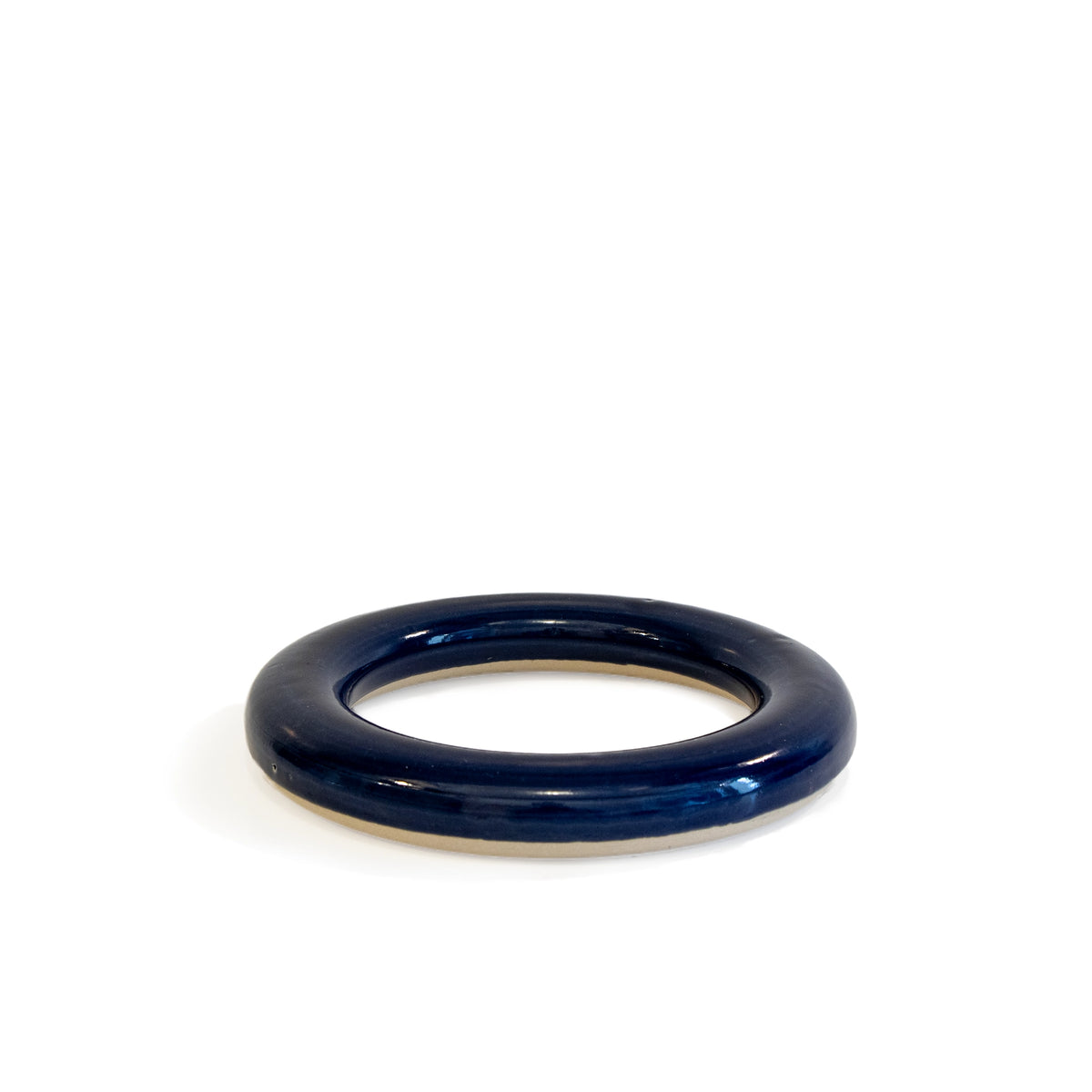 De AB Ceramics Pot Onderzetter Blauw D16,5, een glanzend donkerblauw keramisch onderzetter met een minimalistisch ontwerp van AB Ceramics, ligt plat op een wit oppervlak, waarbij de gladde ronde vorm een zachte schaduw werpt onder het open midden.
