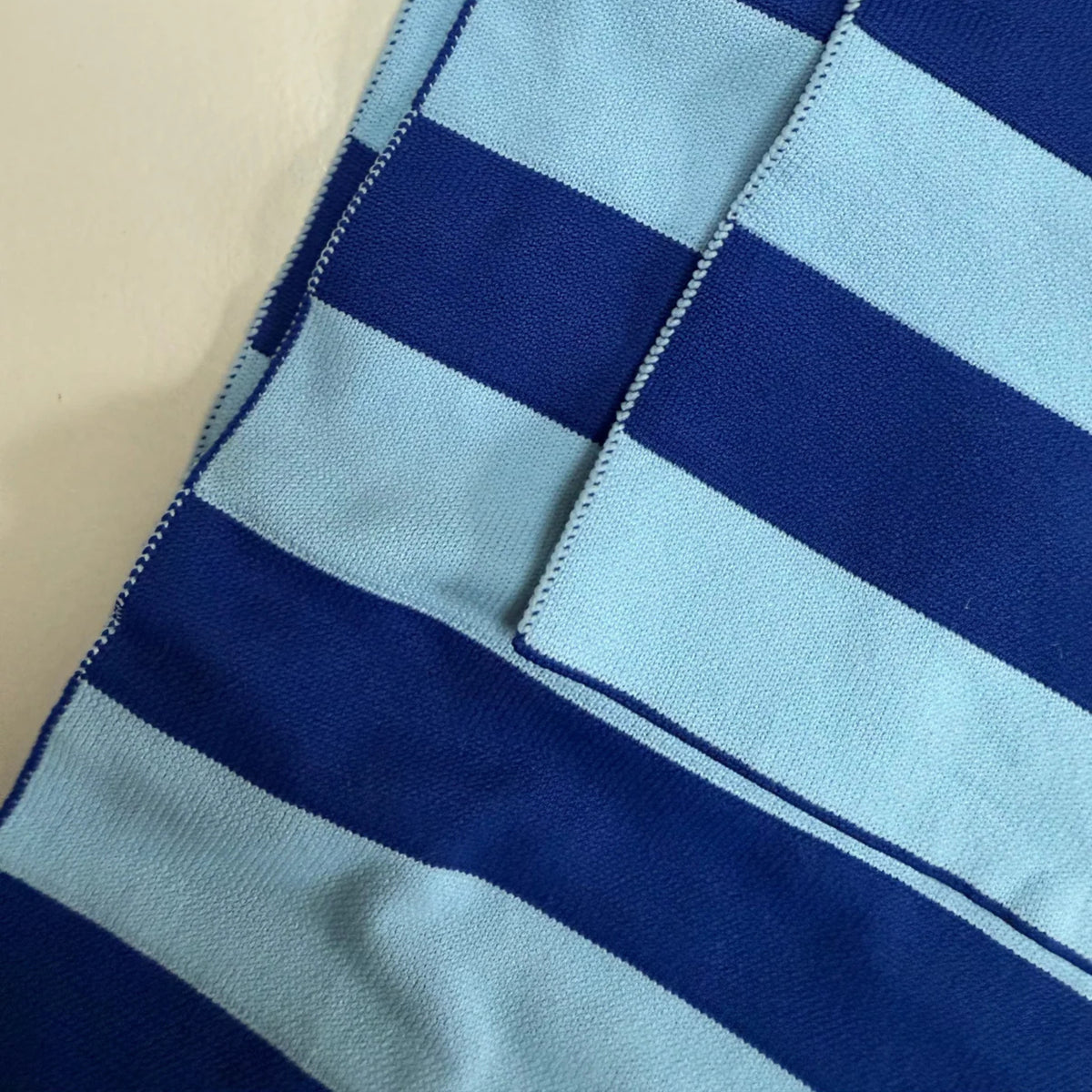 Close-up van de Caro Antwerp Caro Sjaal Ace Ice Ice Baby stof, met horizontale lichtblauwe en donkerblauwe strepen met een overlappende naad en zichtbare stiksels.
