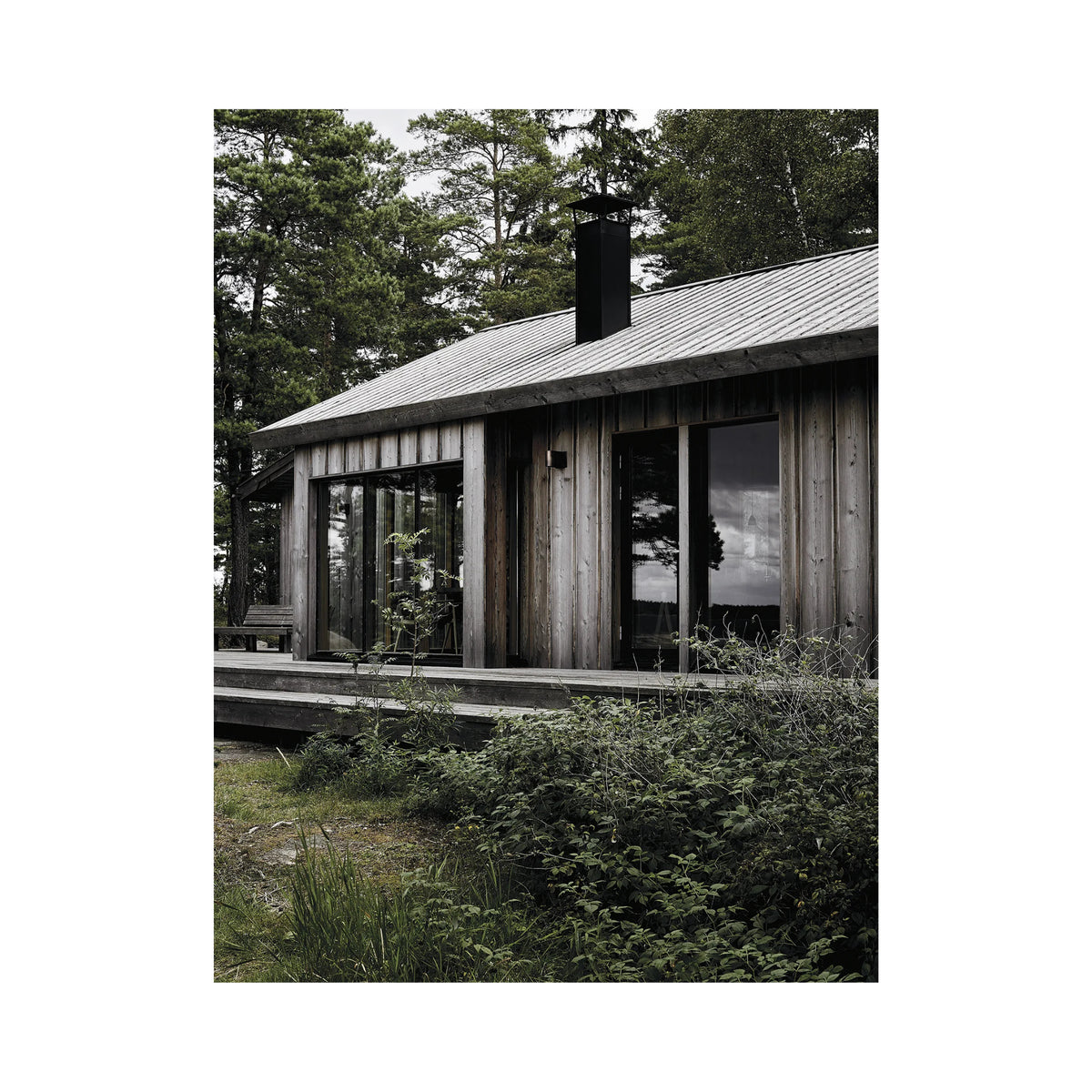 Een moderne houten hut met grote ramen en een metalen schoorsteen staat op een dek tussen hoge bomen, zoals te zien is in het boek Happy Homes Hideaways van Cozy Publishing.