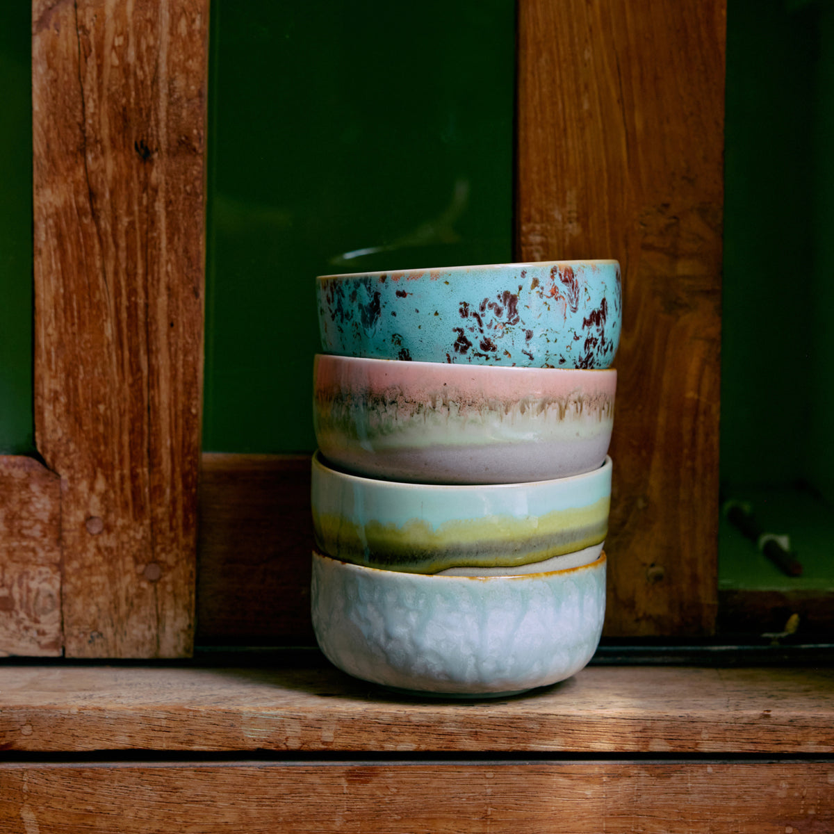 De HK Living 70s Ceramics Dessertkom Impression set van 4 kommen, elk met unieke pastelpatronen, is gestapeld op een rustieke houten vensterbank tegen weelderig groen.