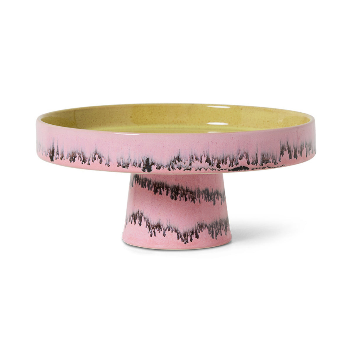 De HK Living 70s Ceramics Kom op Voet Bubble taartstandaard heeft een breed, plat geel oppervlak met een roze glazuur en een zwart druppelpatroon op de rand en basis, wat de kenmerkende jaren 70 stijl van HK Living weerspiegelt.