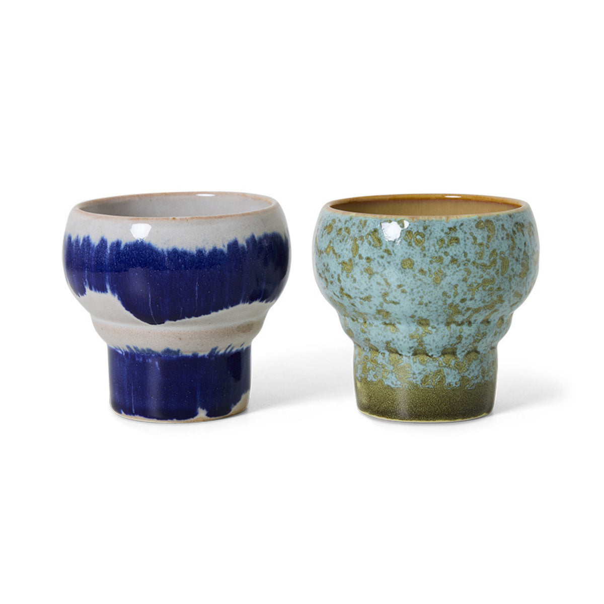 De HK Living 70s Ceramics Lungo Mokken Symbolist set bestaat uit twee moderne, ambachtelijke mokken van keramiek: de ene glanzend blauw met wit, de andere gespikkeld lichtgroen met bruin, beide met brede randen in ware HK Living stijl.