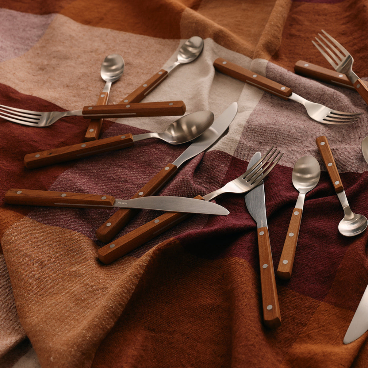 Een set HK Living 70s Cutlery tafellepels met houten handgrepen is verdeeld over een bruin en roest geruite stof, die de retro charme en vintage stijl van 70s bestek weerspiegelt.