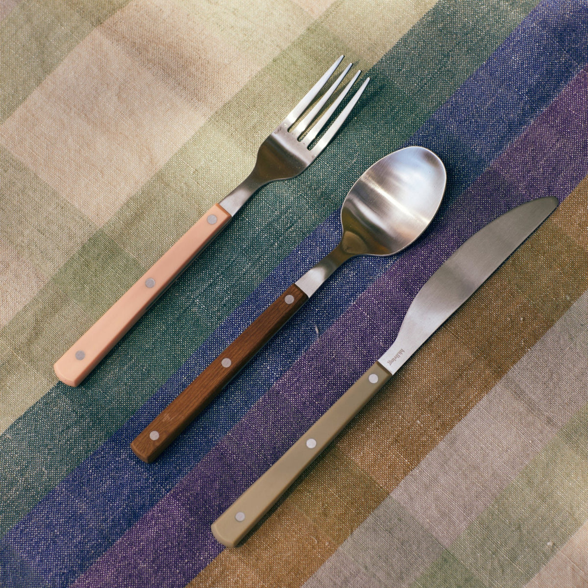 Het HK Living 70s Tafelvork Olijfgroen bestek heeft een stijlvol, retro olijfgroen handvat, gerangschikt op een levendig geruit doek om het speelse 70s design van HK Living te laten zien.
