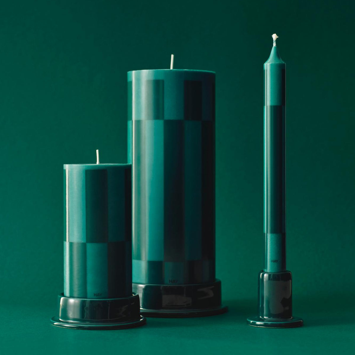 Hay Patroon Kaarsen Groen en Bordeaux (set van 4) van Hay: decoratieve kaarsen met geometrische patronen op bijpassende houders, perfect als stijlvol cadeau tegen een groene achtergrond.