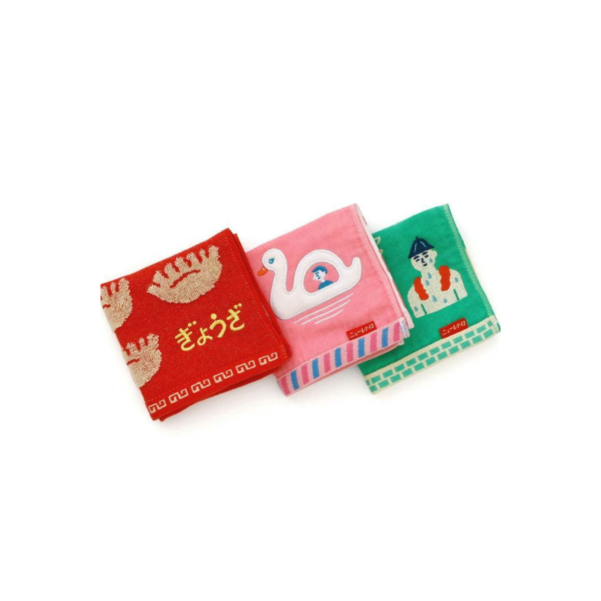Drie Hightide Handdoek Dumpling 25/25 handdoeken liggen naast elkaar: op de rode staan krabben met Japanse tekst, op de roze staat een zwaan in het zwembad en op de groene staat een persoon met een hoed en een zandkasteel.