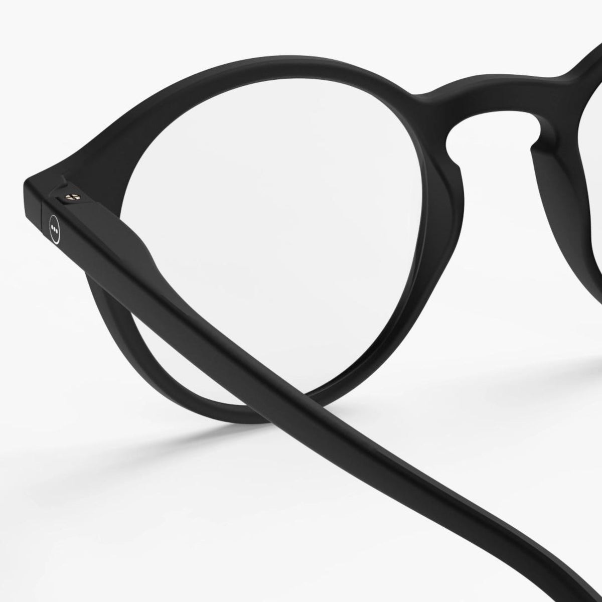 Close-up van de Izipizi Leesbril #D Zwart met heldere glazen, met het zwarte ronde montuur en de veren tegen een effen witte achtergrond - perfect voor mensen met ouderdomsverziendheid.