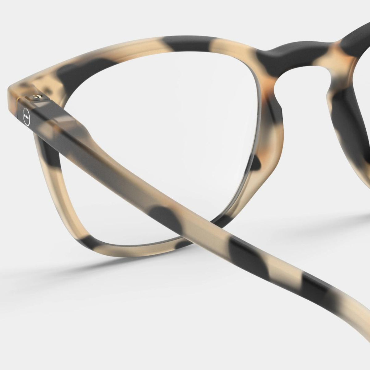 Close-up van de Izipizi Leesbril #E Light Tortoise van Izipizi, een stijlvolle leesbril in schildpad beige, bruine en zwarte tinten voor mannen en vrouwen, afgebeeld tegen een effen lichte achtergrond.