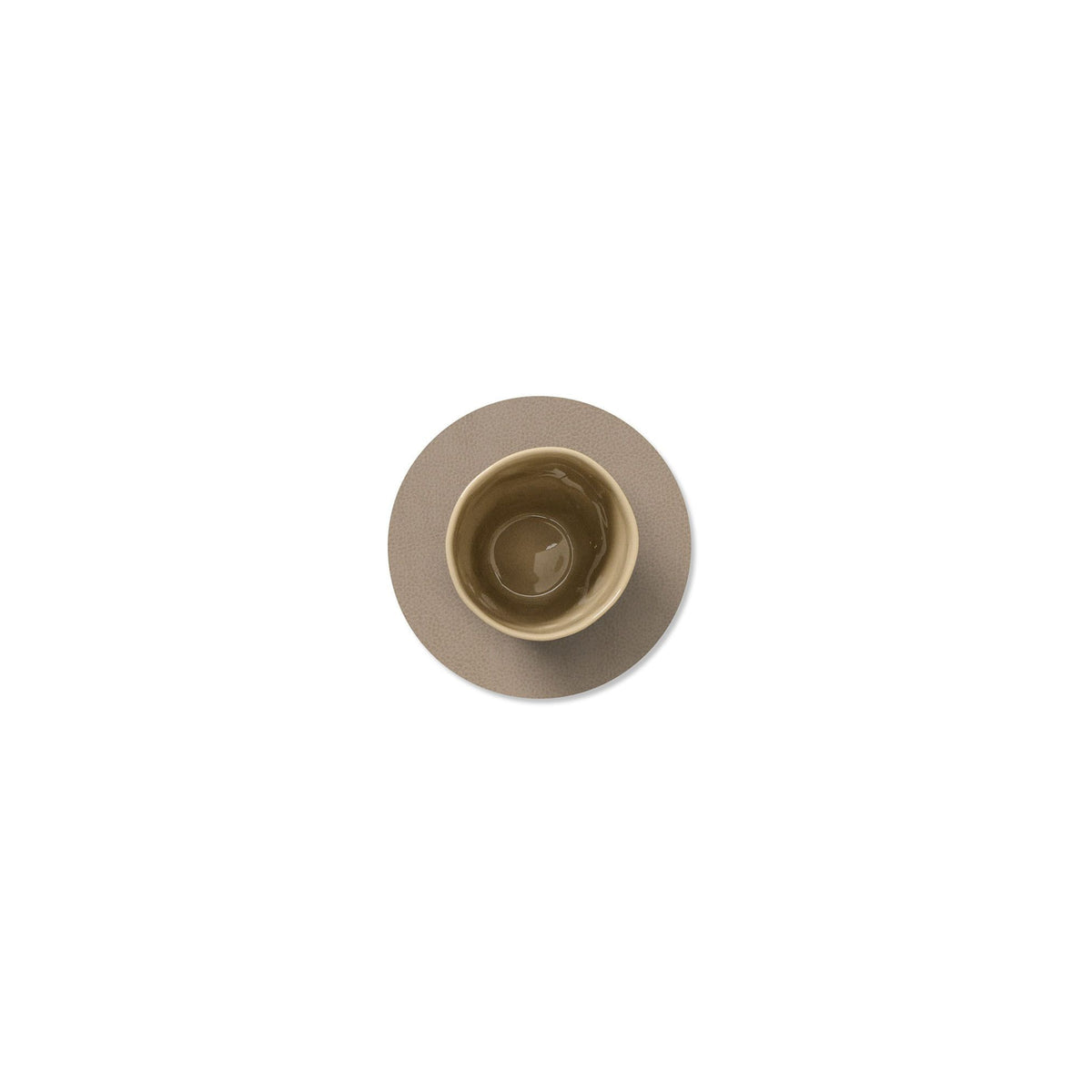 Een beige keramische kop met water staat op een bijpassende schotel, geplaatst op de Lind DNA Serene Onderzetter Rond Molgrijs D10 van Lind DNA, van bovenaf afgebeeld op een effen witte achtergrond.