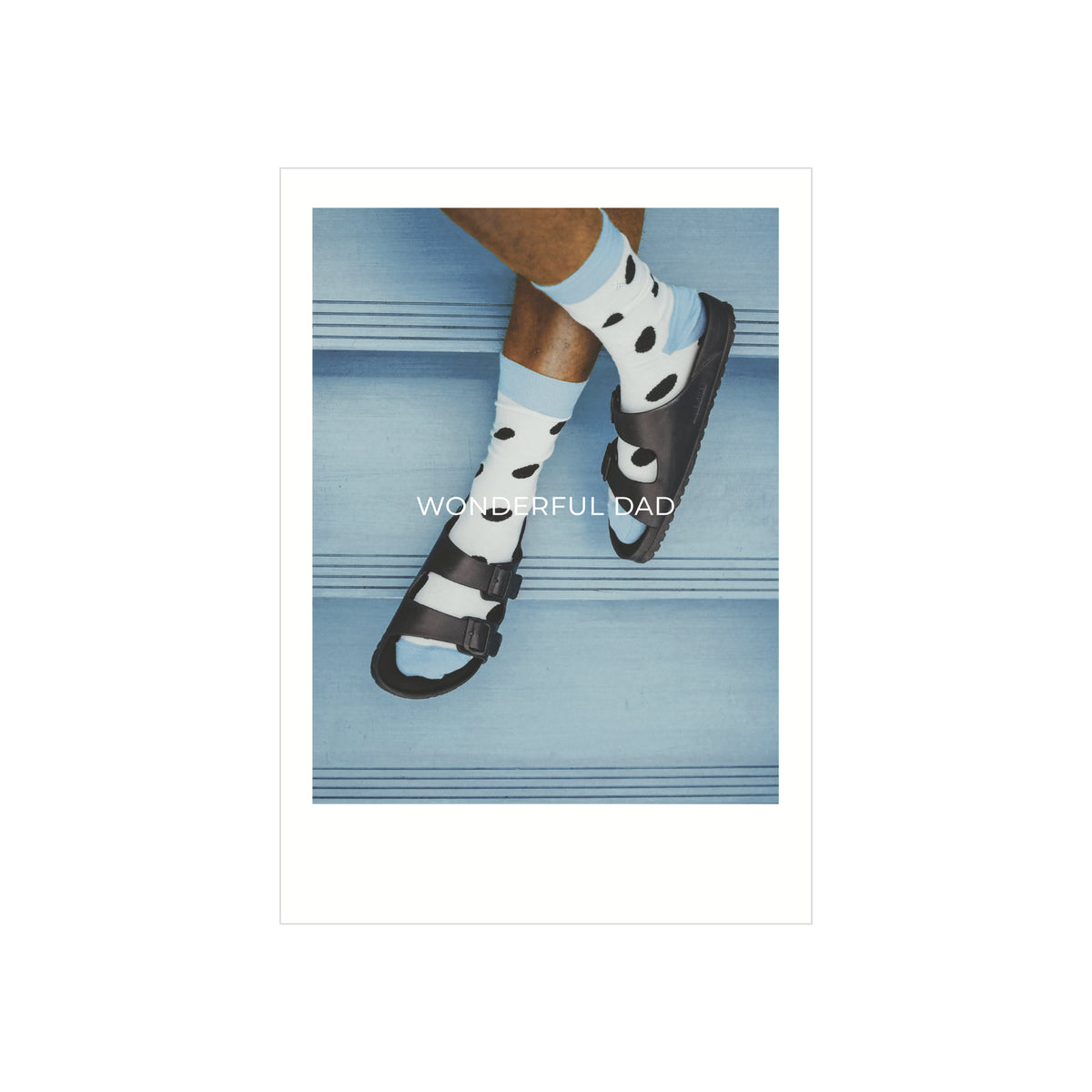 Een persoon in zwarte sandalen en lichtblauwe sokken met zwarte stippen zit op blauwe traptreden. "WONDERFUL DAD" is gedrukt op deze Matriks Postkaart Polaroid Wonderful Dad Dubbel A6 van Matriks.