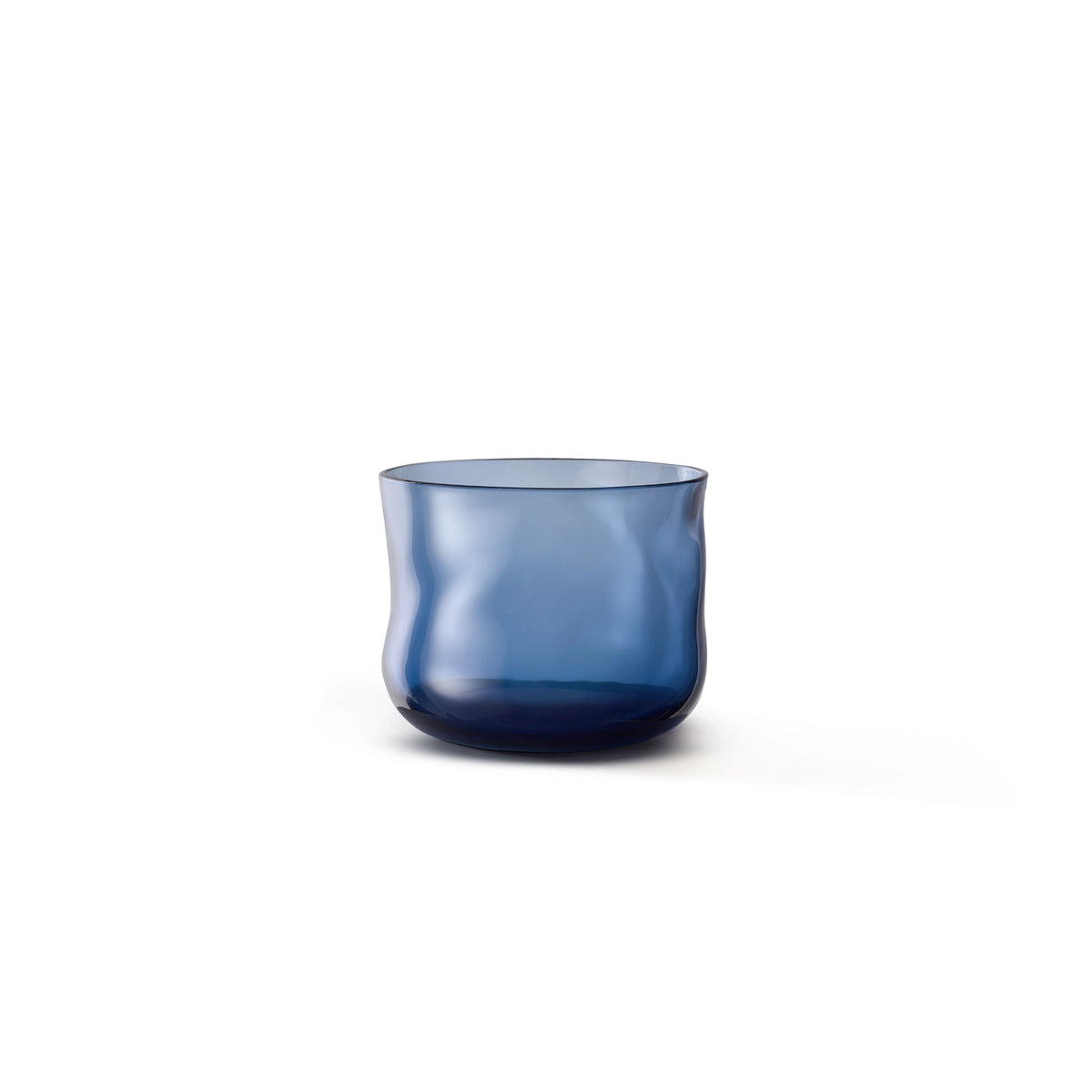 De Paveau Swirl Waterglas Midnight Blauw 24 cl van Paveau is een doorschijnende donkerblauwe glazen beker met een organische golvende vorm, elegant afgebeeld tegen een witte achtergrond.