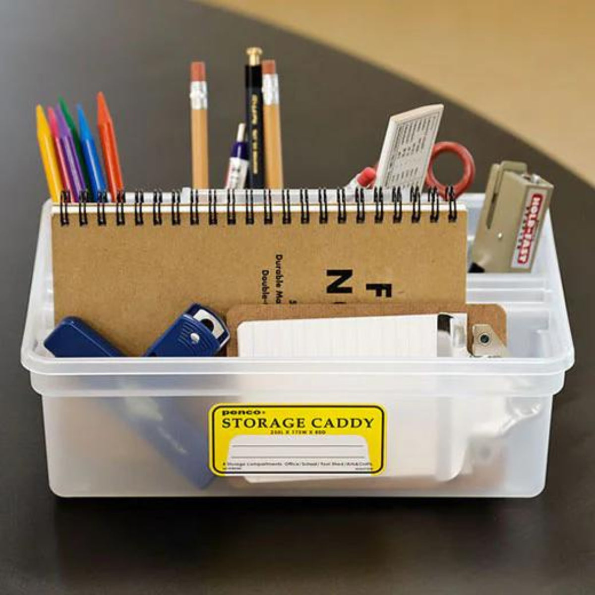De Penco Opbergcaddy Helder van Penco organiseert gekleurde pennen, potloden, scharen, een nietmachine, notitieblok, indexkaarten en kantoorbenodigdheden. Het heeft een doorzichtig ontwerp met een geel "Storage Caddy" label op de voorkant.