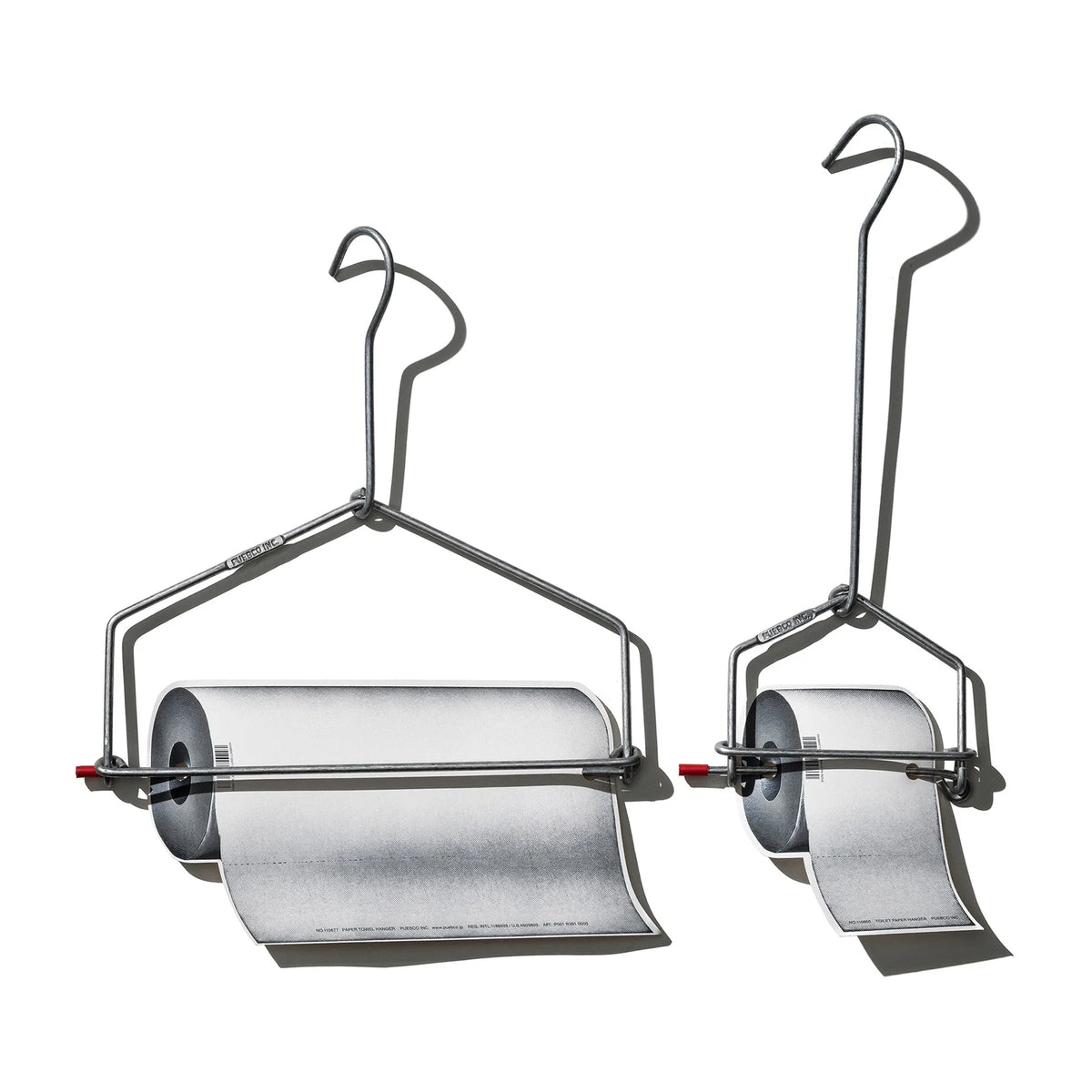 Twee metalen Puebco Keukenrolhouderhangers houden elk een papierrol vast die naar beneden rolt tegen een witte achtergrond, met sterke schaduwen naar rechts.