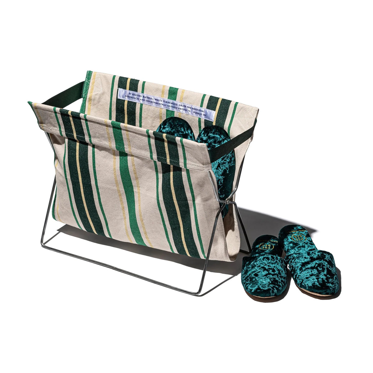 De Puebco Magazinehouder Café Groen Strepen, een gestreepte stoffen houder met een stalen frame, zit naast groene fluwelen slippers - een stijlvolle en milieuvriendelijke touch voor je organisatie.