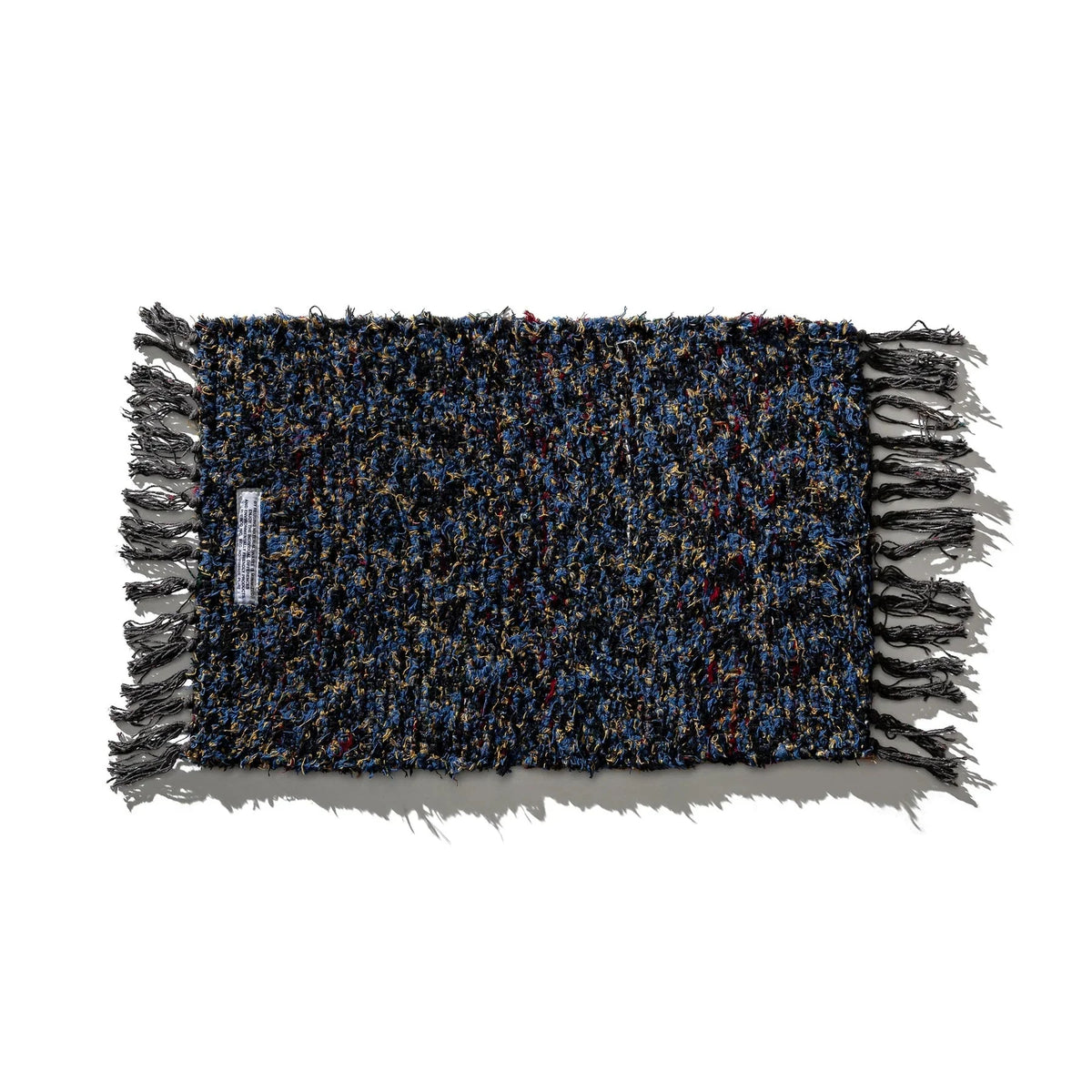 De Puebco Mat Gerecycleerd Textiel 63/41 is een rechthoekige mat van Puebco met veelkleurige blauwe, zwarte en gouden draden en gefranjerde randen, plat uitgelegd op een witte ondergrond.