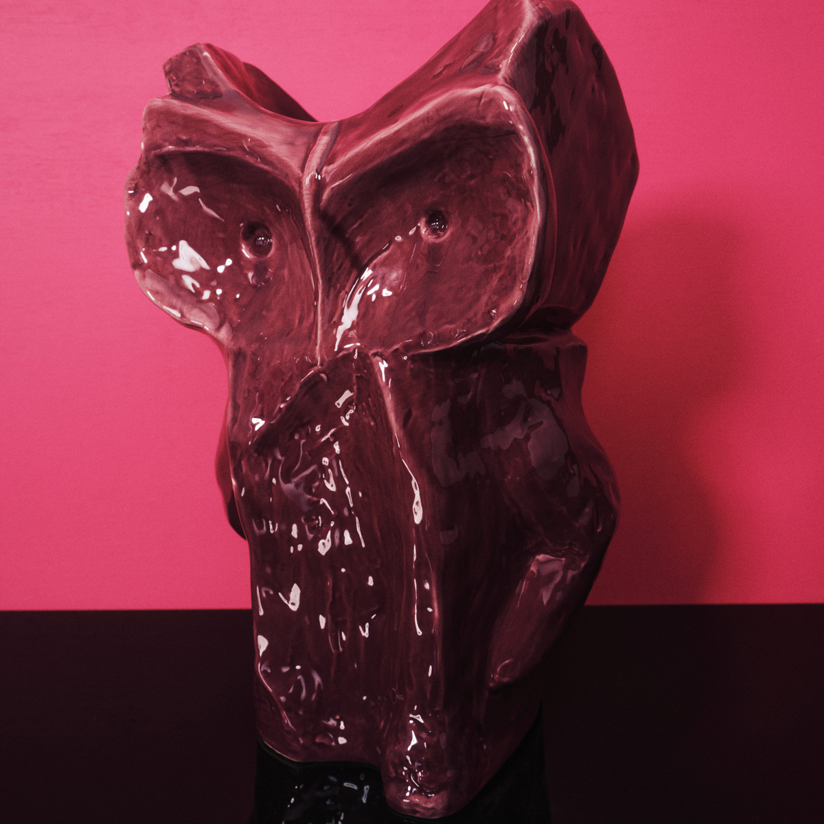 Een glanzend, abstract keramiek Serax After Midnight Uil Vaas Aubergine L staat tegen een roze achtergrond en donker oppervlak, met gestructureerde details en dieprode tinten.