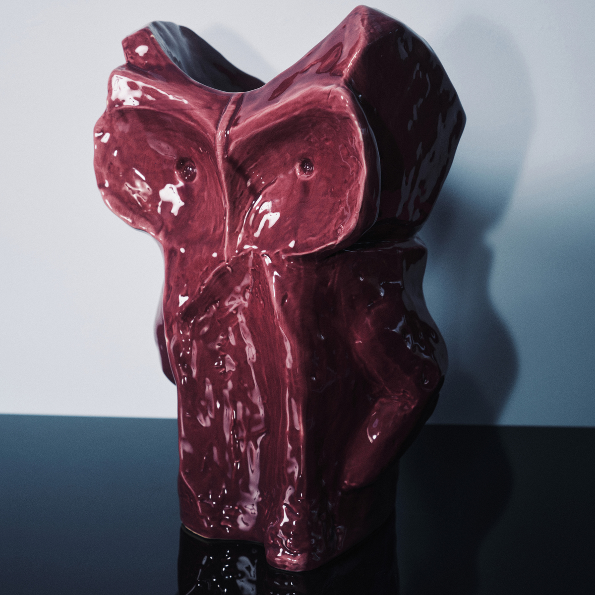 Een glanzend, diep aubergine Serax After Midnight Uil Vaas L keramisch beeld staat op een reflecterend zwart oppervlak, tegen een effen lichte achtergrond.