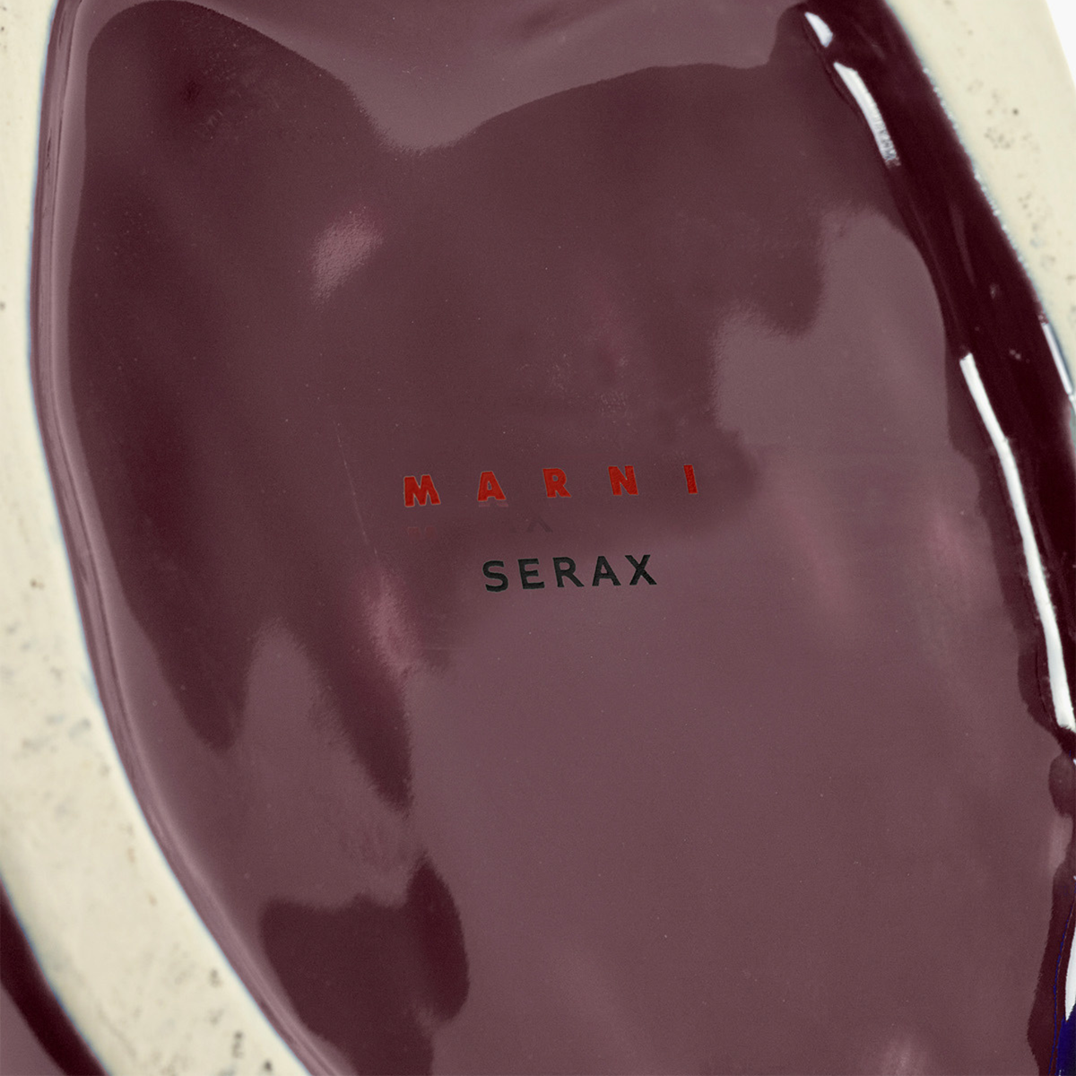 Close-up van het glanzende, aubergine keramische oppervlak van de Serax After Midnight Uil Vaas Aubergine L, met "SERAX" in zwarte en rode letters in het midden.
