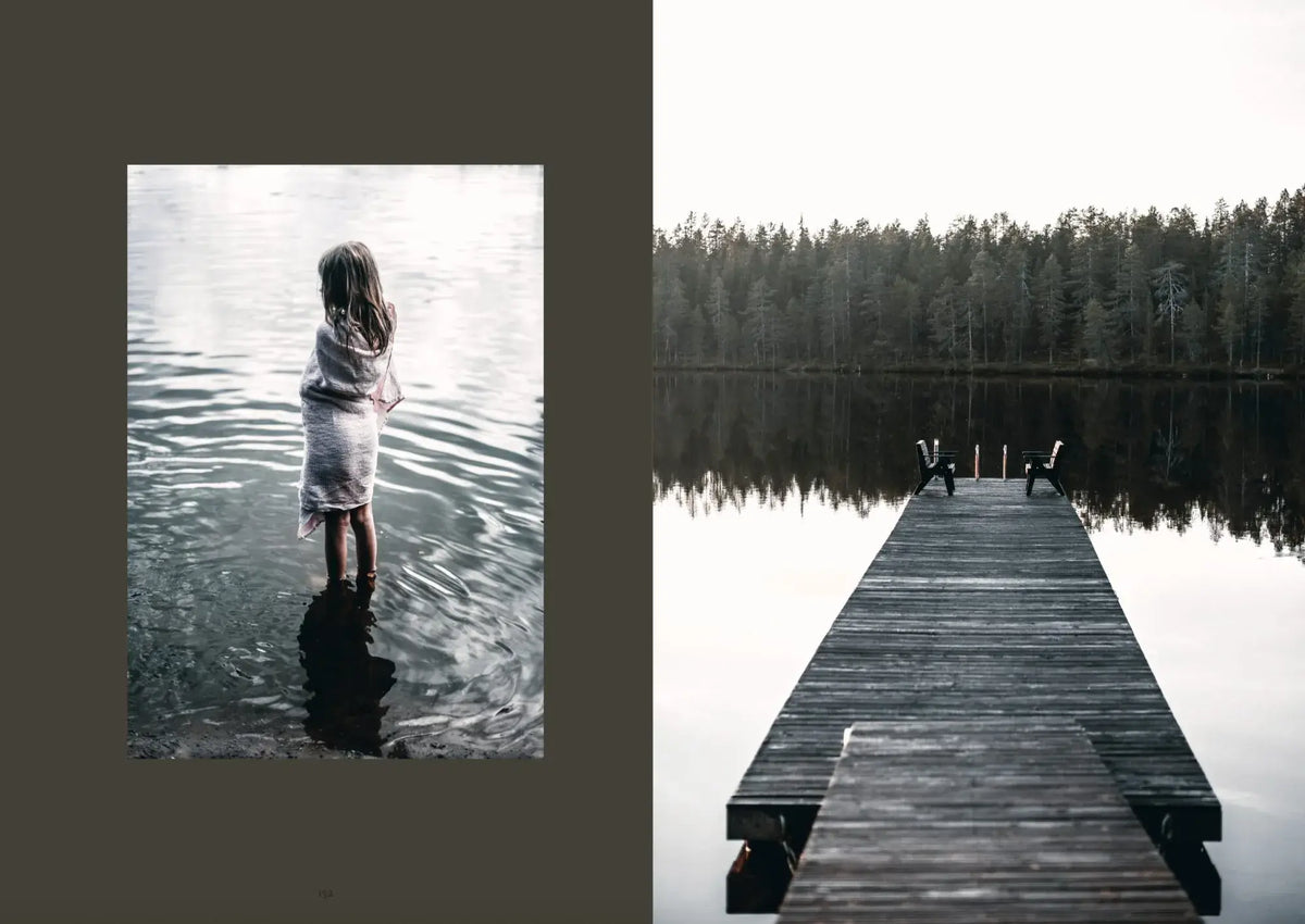 Een meisje in een handdoek staat in ondiep water, wat sauna wellness oproept, terwijl een houten steiger zich uitstrekt over een kalm meer - een beeld dat de rustige geest vastlegt in het Sauna Boek van Cozy Publishing.