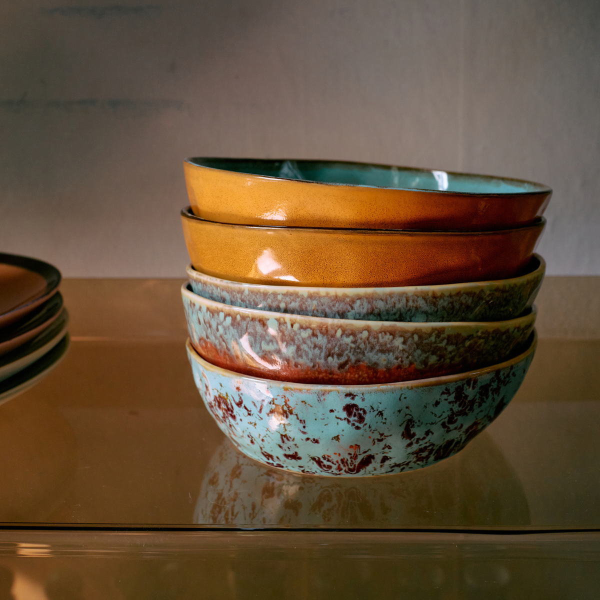 Twee HK Living 70s Ceramics Pasta Kom Patina kommen in aardetinten turquoise en bruin staan op een glazen plank tegen een neutrale achtergrond.