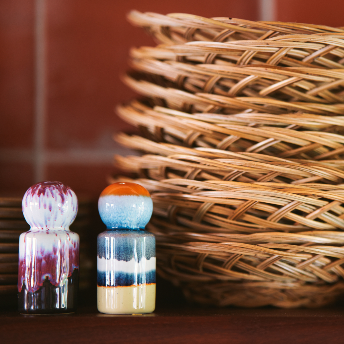 De HK Living 70s Ceramics Peper- en Zoutvaatje Stargaze 2 st. set voegt een retro touch toe naast gevlochten rieten manden op roodachtige tegels - perfecte tafelaccessoires om je keuken op te fleuren.