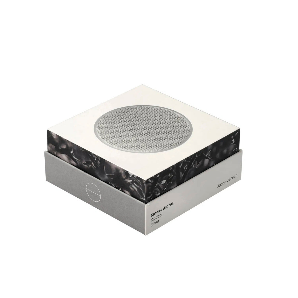 De Jacob Jensen Optical Rookmelder Zilver D10 heeft een Scandinavisch ontwerp, met een vierkante vorm, een slanke witte en grijze verpakking en een ronde sensor van zilvergaas bovenop, tegen een effen witte achtergrond.