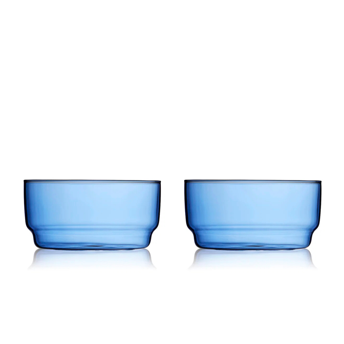 Twee Lyngby Glas Torino Kom Blauw D12 kommen (set van 2) staan naast elkaar op een witte achtergrond en laten het eenvoudige, ronde ontwerp en de gladde oppervlakken van borosilicaatglas zien.