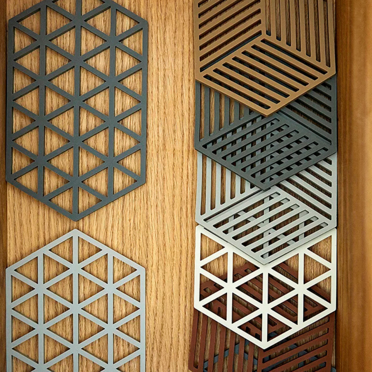 Zeshoekige metalen patronen met geometrische uitsparingen in driehoekige en gestreepte ontwerpen sieren de Zone Denmark Hexagon Trivet Olijfgroen-een stijlvolle olijfgroen onderzetter van Zone Denmark voor moderne tafelbladen.