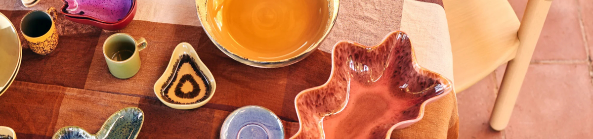 Op een ronde tafel met een wit tafelkleed liggen frambozen, een brood, een kaars, een glazen fles met water en verschillende decoratieve schalen en voorwerpen tegen een lichtblauwe achtergrond.