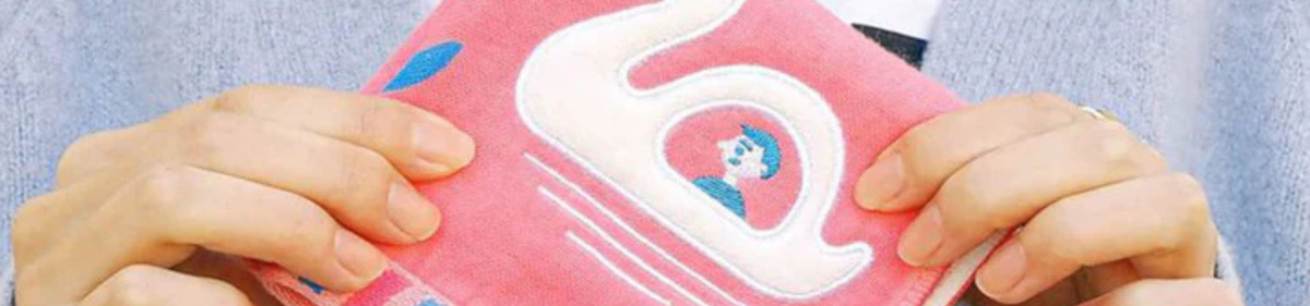Een persoon die een roze doek met een witte zwaan en een klein blauw en wit figuurtje vasthoudt en een lichtblauwe trui draagt.