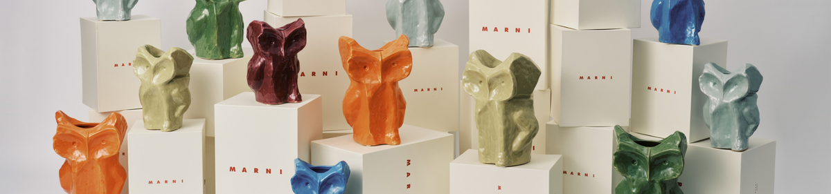 Vaasjes van keramiek in de vorm van dieren in groen, oranje, rood, grijs en blauw staan op witte dozen van het Marni-merk op verschillende hoogtes.