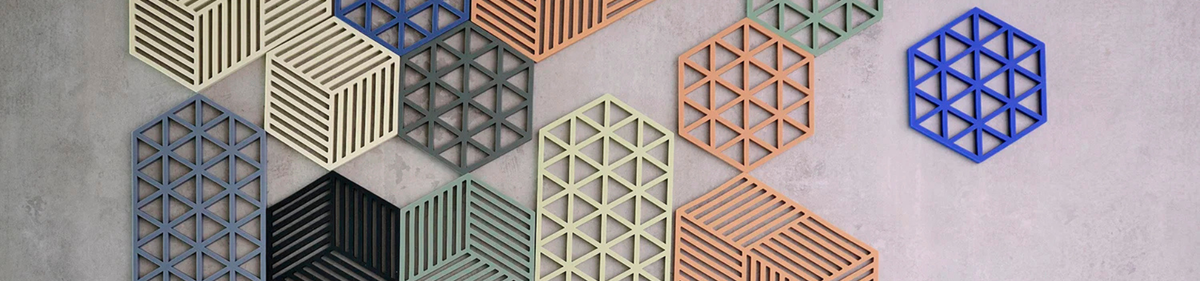 Geometrische muurkunst met zeshoekige vormen in verschillende kleuren en patronen, gerangschikt op een lichtgrijze muur met structuur. De vormen hebben open, rastervormige ontwerpen.