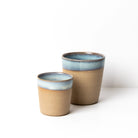 Het AB Ceramics Espressokopje Geel Opaal/Blauw 10 cl heeft twee keramieken kopjes - een klein, handgegoten kopje in geel opaal met een blauwe rand, met uniek handgemaakt servies van AB Ceramics tegen een effen witte achtergrond.
