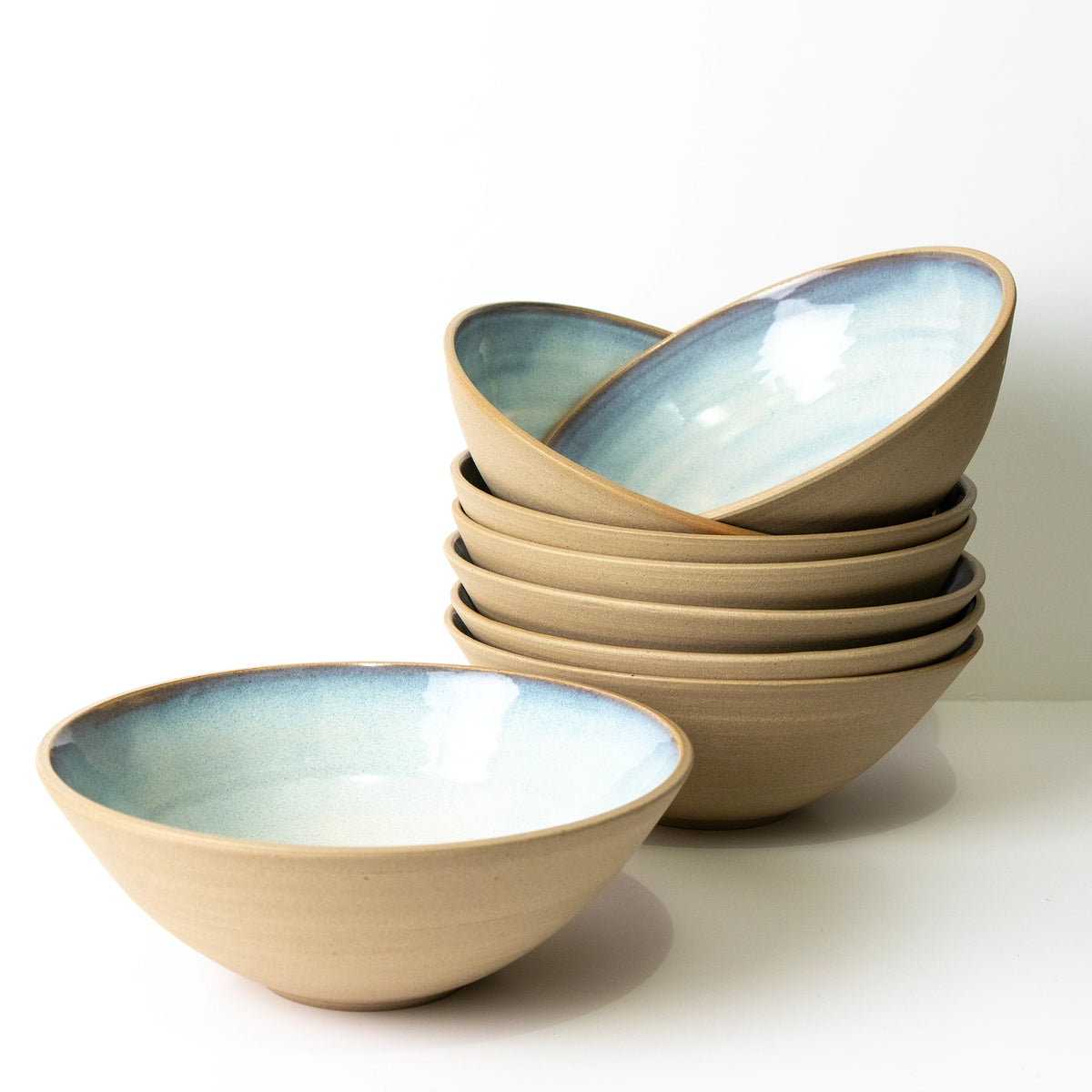 Een stapeltje van zes AB Ceramics Noodle Kom Geel Opaal D19 kommen met een matte bruine buitenkant en glanzende lichtblauwe binnenkant - ideaal als noodle bowl set voor je AB Ceramics handgemaakte serviescollectie.