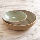 Op een marmeren oppervlak: een kleinere, glanzend groene AB Ceramics Noodle Kom Wit Mint D19 genesteld in een grotere, matbeige kom met een onafgewerkte rand.