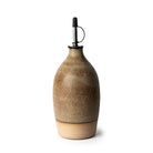 De AB Ceramics Olijfolie Fles 2 Toffee Mos 65 cl is een handgedraaid keramiek fles met bruin-beige gespikkelde glazuur, metalen schenktuit en zwarte stopper-stijlvol als keuken decoratie, gepresenteerd tegen een witte achtergrond.