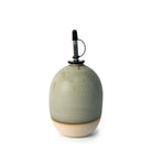 De AB Ceramics Olijfolie Fles Wit Mos 60 cl heeft een rond, handgegoten keramisch ontwerp met een mat lichtgroen glazuur en een beige basis, met daarop een metalen en zwart rubberen schenktuit - een elegant AB Ceramics keukenaccessoire tegen een witte achtergrond.