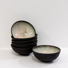 Links staan vijf AB Ceramics Mini Kom Zwart Opaal D10,5 kommen met een glanzende binnenkant, rechts één op zichzelf staande kom tegen een effen witte achtergrond.