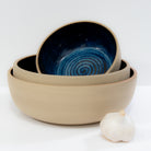 De AB Ceramics Serveerschaal Spiraal Geel Blauw D22,5, met een blauw spiraalpatroon binnenin, wordt weergegeven naast een knoflookbol op een wit oppervlak met een effen witte achtergrond.