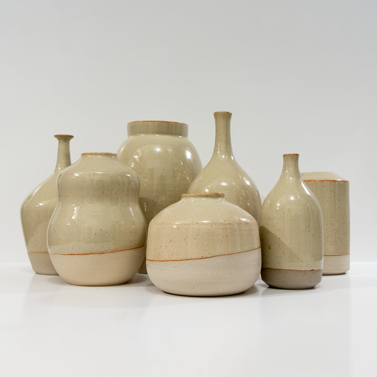 Een groep beige keramische vazen en potten, waaronder de AB Ceramics Vaas Geel Beige H20,5 van AB Ceramics, gerangschikt op een wit oppervlak tegen een effen witte achtergrond.