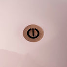 Een close-up van een zwart machtssymbool als een verticale lijn in een cirkel op lichtroze, perfect passend bij de zachte gloed van sfeerverlichting of de Addison Ross Bobbin Lamp LED Oplaadbaar Roze.
