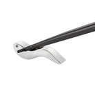 Een paar Alessi Anna eetstokjes rust op een slanke, zilveren vogelvormige houder tegen een witte achtergrond - een elegant tafelaccessoire van Alessi.