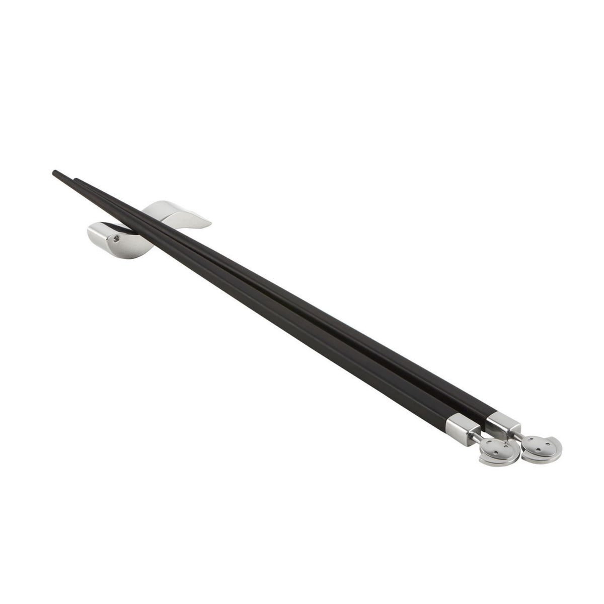 Een paar zwarte Alessi Anna eetstokjes met zilveren uiteinden en lachende gezichtjes rusten op een slanke, walvisvormige houder - een elegant voorbeeld van Alessi's speelse tafelaccessoires design.