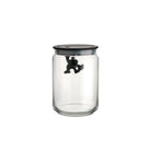 De Alessi Gianni Voorraadpot Zwart 90 cl van Alessi heeft een heldere pot met een zwart deksel, waar een klein zwart apenfiguurtje aan de onderkant hangt. De achtergrond is effen wit.