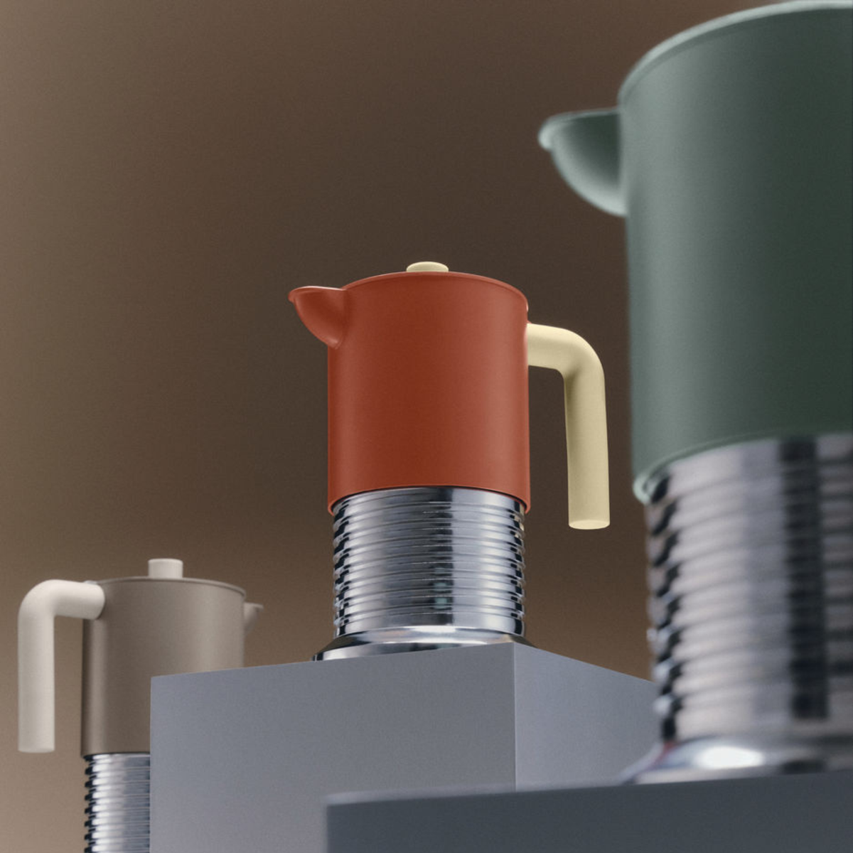 De Alessi Vite Koffiemaker Saliegroen 3-Kops, met een crèmekleurig handvat en metalen voet, staat op verschillende hoogtes naast rode en taupekleurige mokapotten op grijze voetstukken tegen een vage bruine achtergrond.