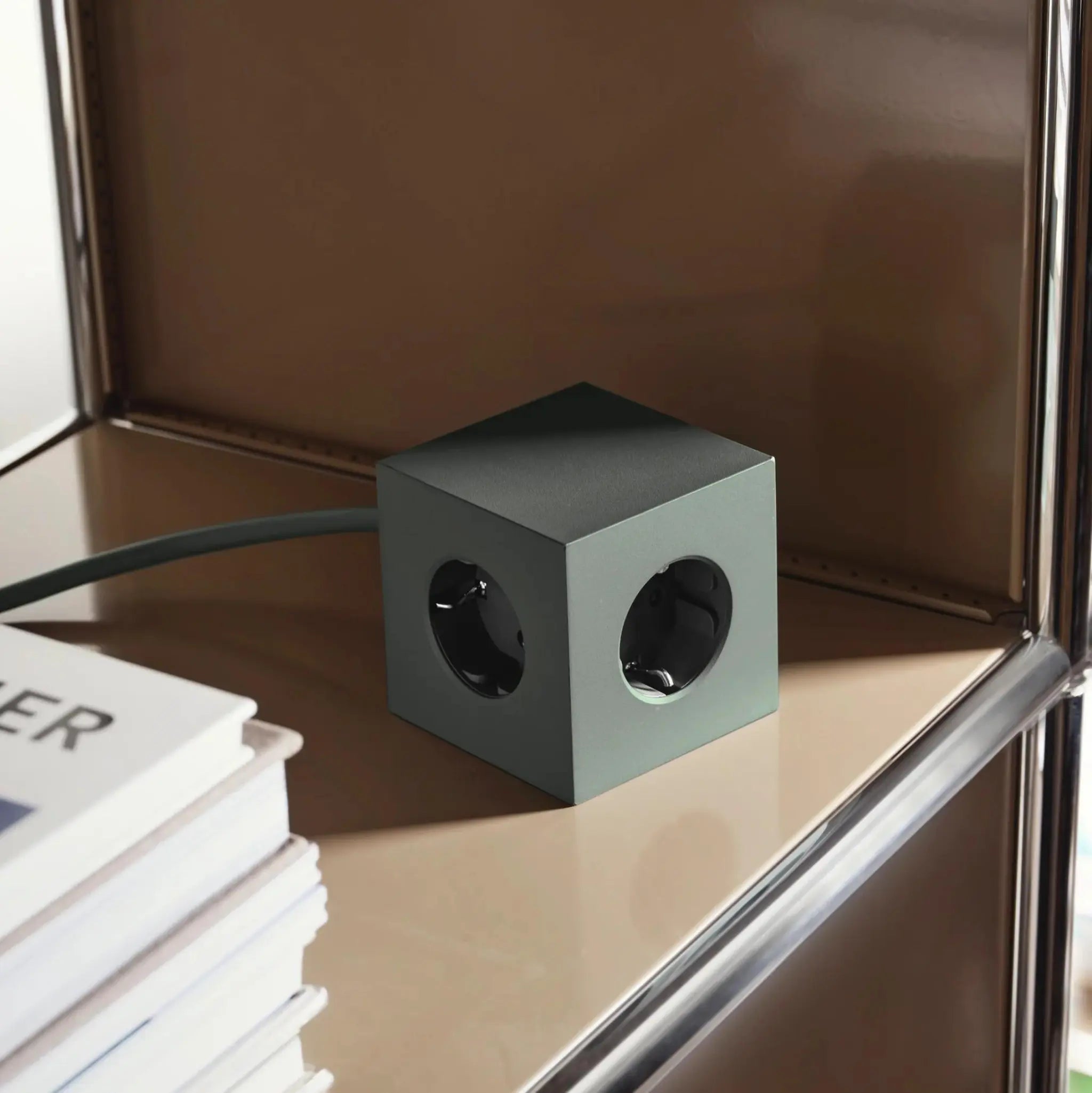 Een Avolt Square 1 USB-C Stekkerdoos Eik Groen 1,8 m van Avolt ligt op een beige plank naast een stapel boeken.
