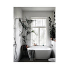 Een moderne badkamer met een wit vrijstaand bad, planten in potten en flessen op de vensterbank toont Scandinavisch design uit het Cozy Publishing Happy Homes Creative Boek, terwijl zonlicht de ruimte vult en een handdoek op het bad rust.