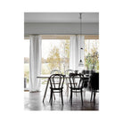 Een minimalistische eetkamer met een witte tafel, zwarte stoelen en grote ramen is gevuld met licht - perfect om het Cozy Publishing Happy Homes Creative Boek door te bladeren in een uitnodigende Scandinavisch geïnspireerde ruimte.
